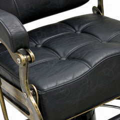 black vintage-style barber chair with quilted padded backrest, adjustable headrest, gold-tone details and footrest